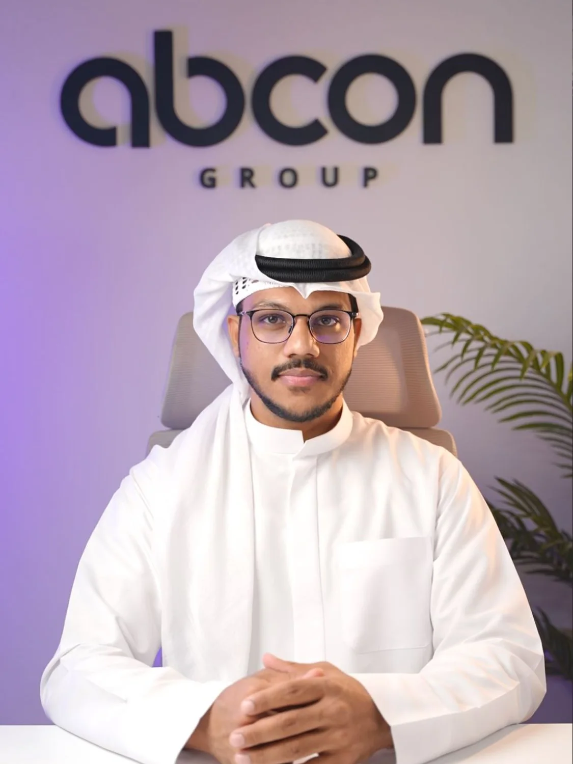 Muhammed Shafad in a white kandura and ghutra, seated at a desk in front of the Abcon Group sign