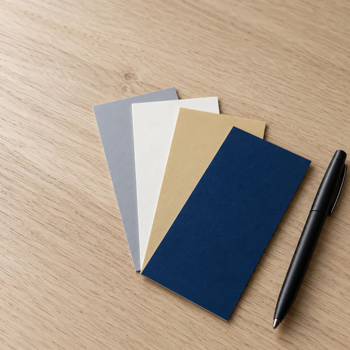 Trus Holding colour swatch chips in navy, gold, white and grey fanned on an oak table beside a black pen