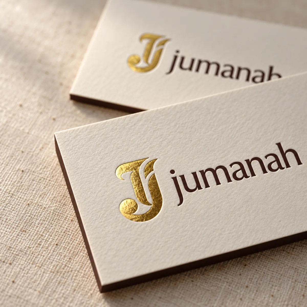Close-up of cream letterpress business cards with a gold foil J monogram and the jumanah wordmark on linen texture.