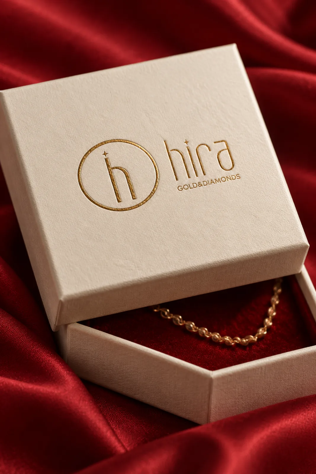 A Hira Gold & Diamonds box with a gold foil logo lifted to show a gold chain on crimson silk