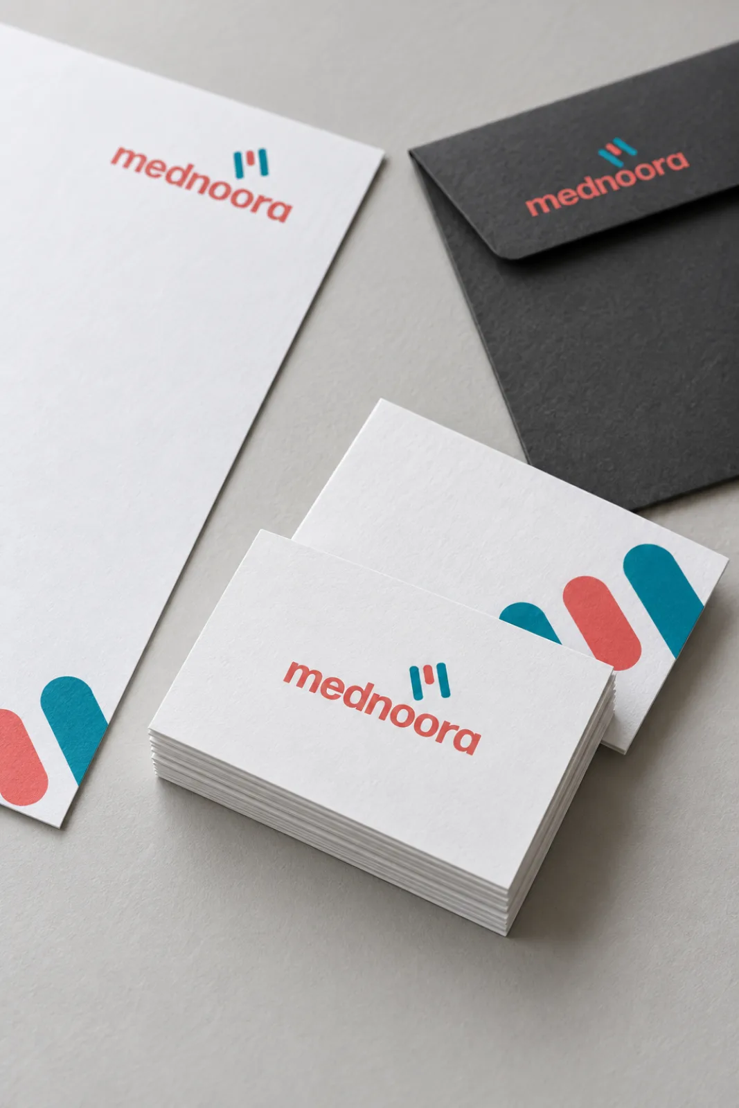Mednoora appointment cards with a coral and teal logo and patterned backs on a grey desk