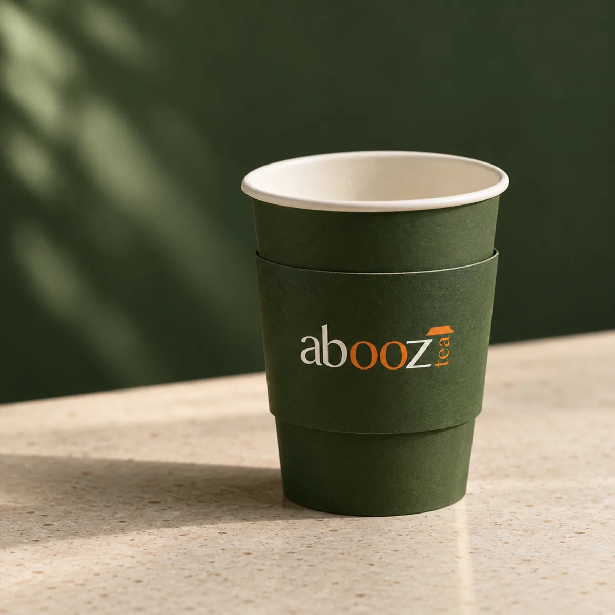 An Abooz paper cup with a green sleeve and logo on a cafe counter