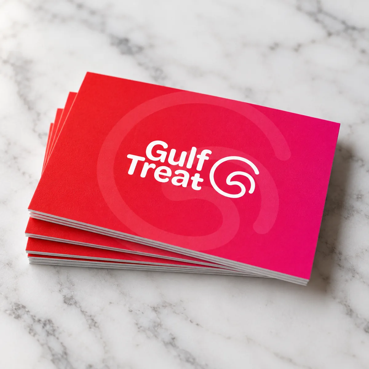 A stack of Gulf Treat business cards with the red to pink gradient on white marble