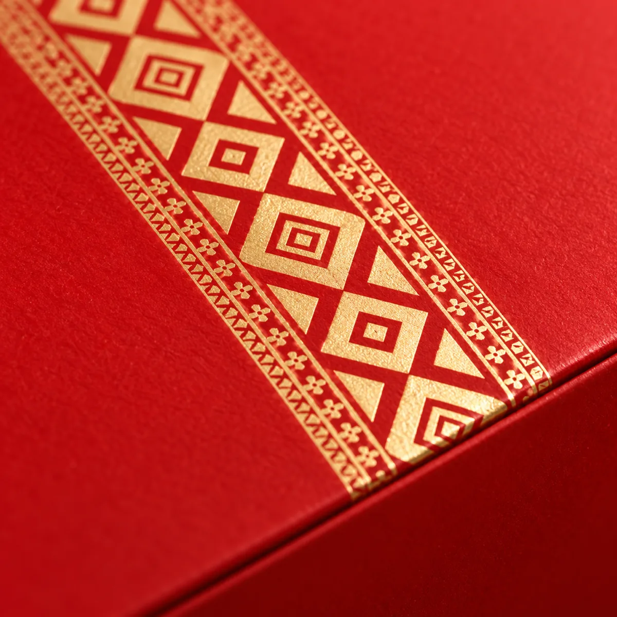 Close-up of gold foil geometric pattern on a red Al Ijaza box lid