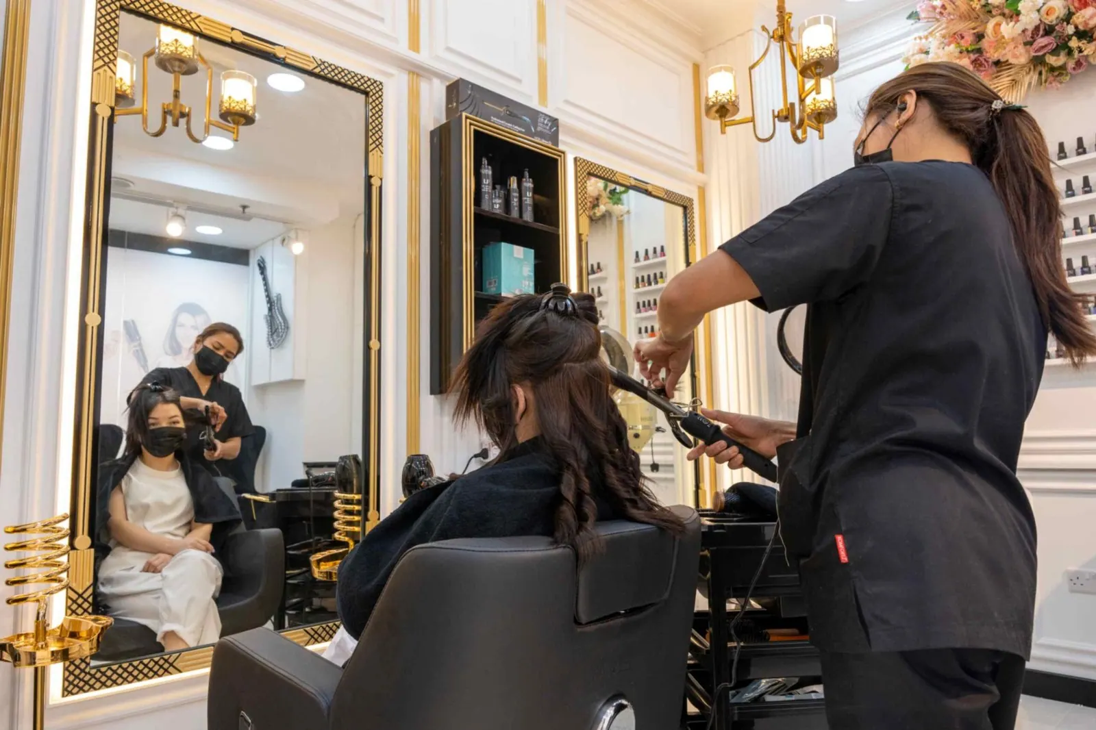 Salon photography: a stylist at work between gold-framed mirrors in a bright room.