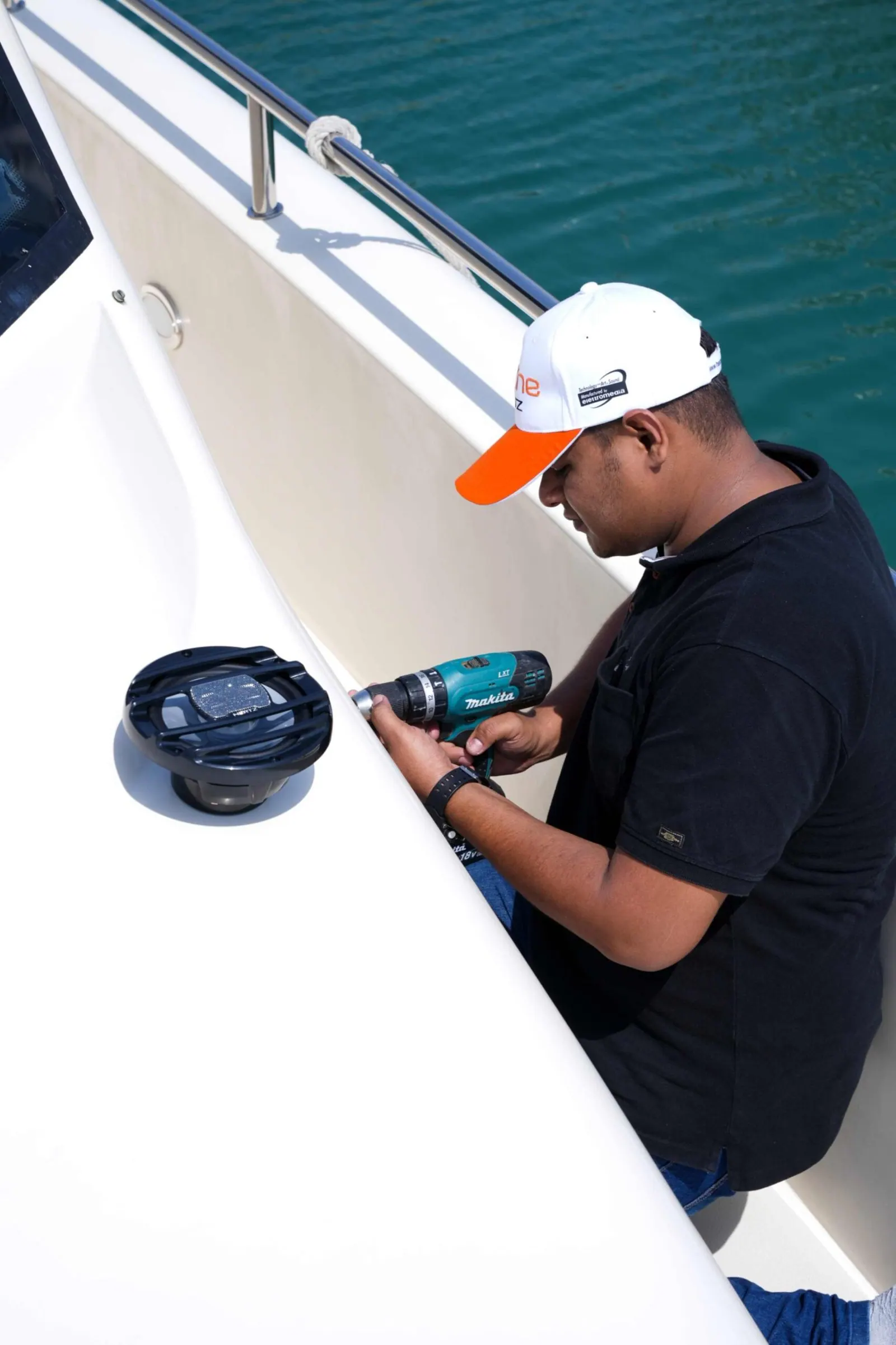 Installation photography: a technician using a handheld drill to fit a speaker to the side of a boat.