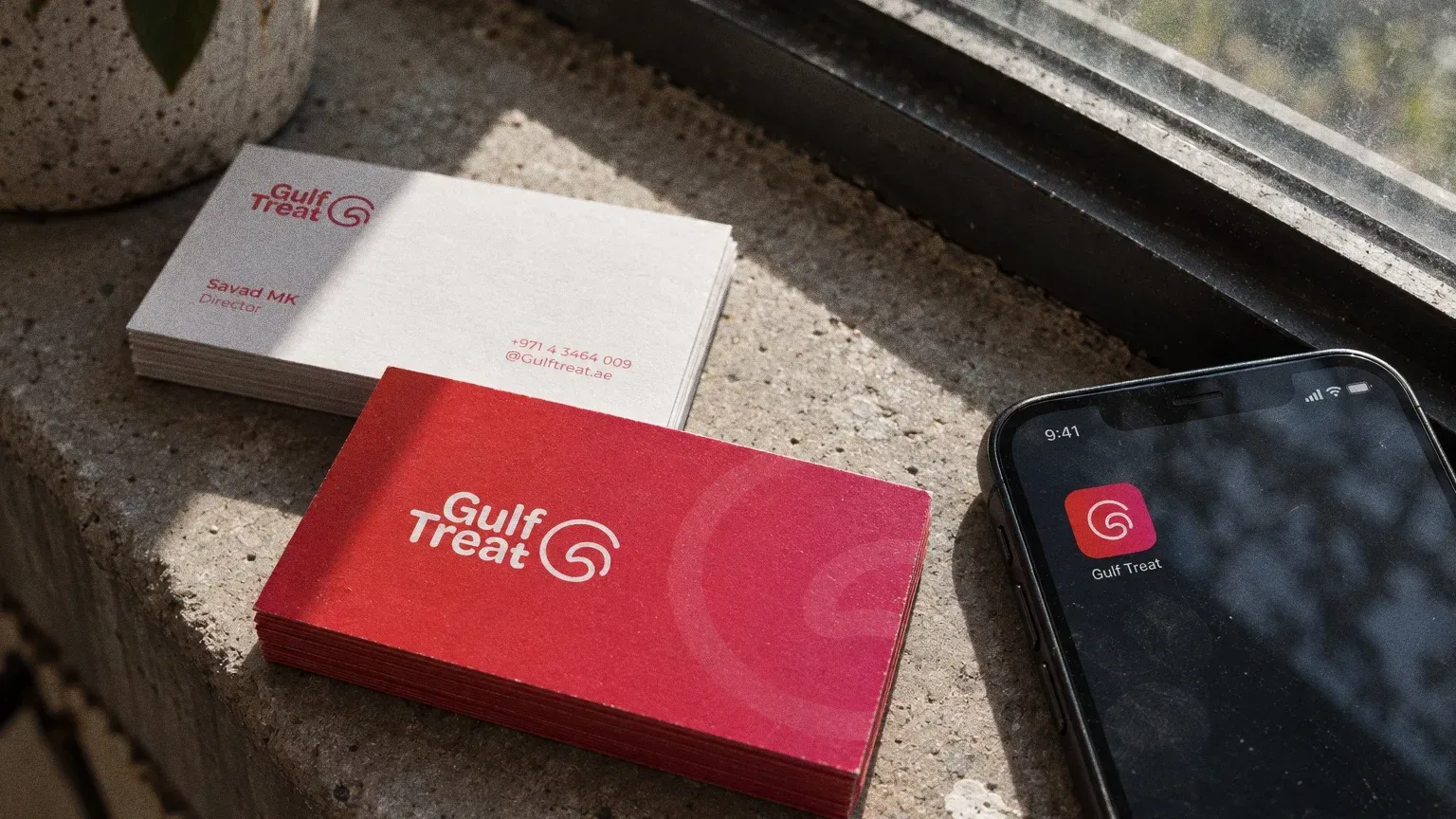 Red gradient and white Gulf Treat business cards on a concrete slab beside a phone showing the app icon.