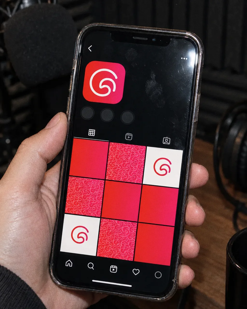 A hand holding a phone that shows a red-to-pink Gulf Treat app icon with the white swirl G and a grid of pattern, solid and symbol tiles.