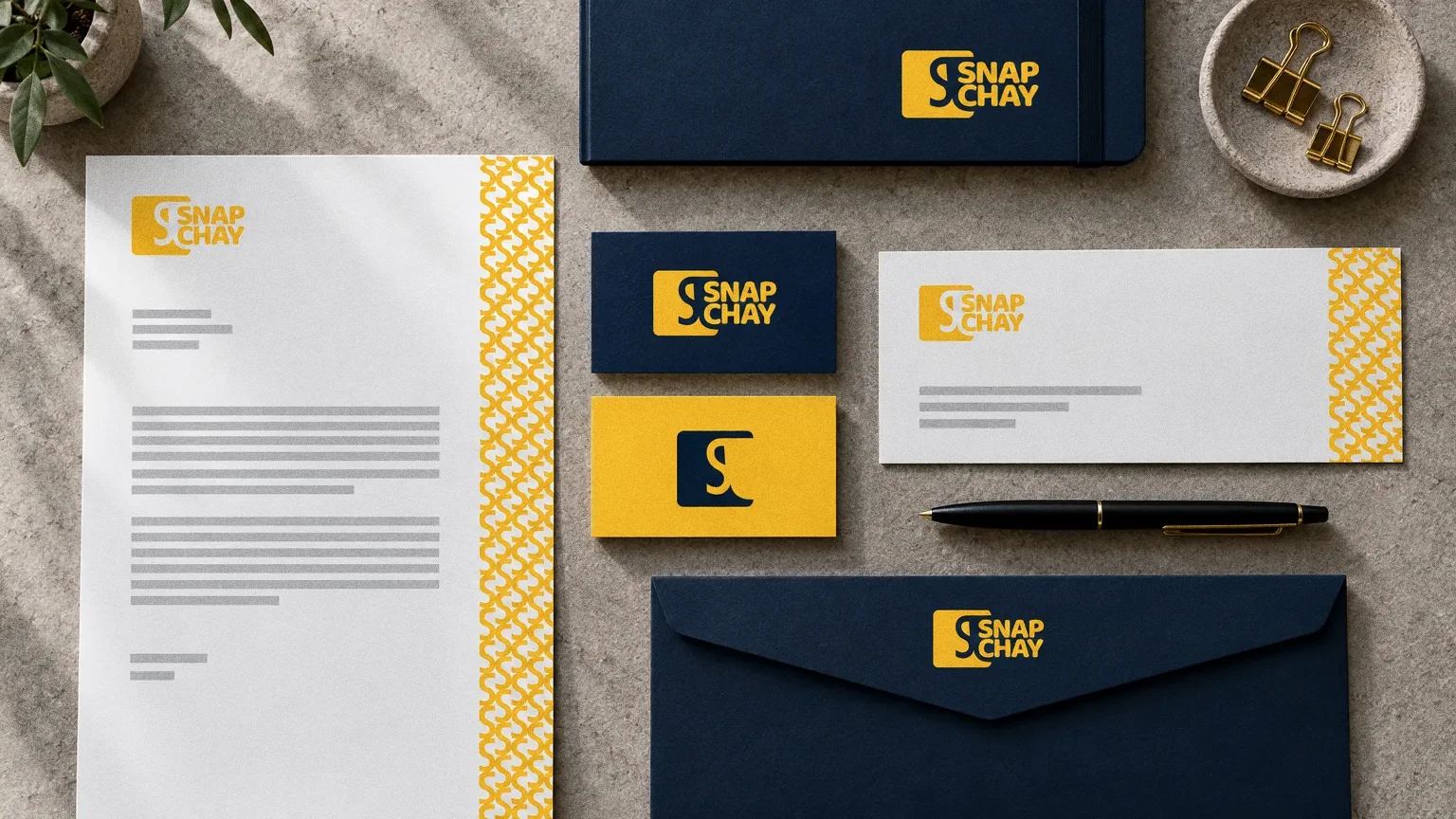 A top-down stationery set on warm grey stone: navy and yellow business cards, a letterhead with a yellow pattern edge, a navy envelope, notebook and pen.