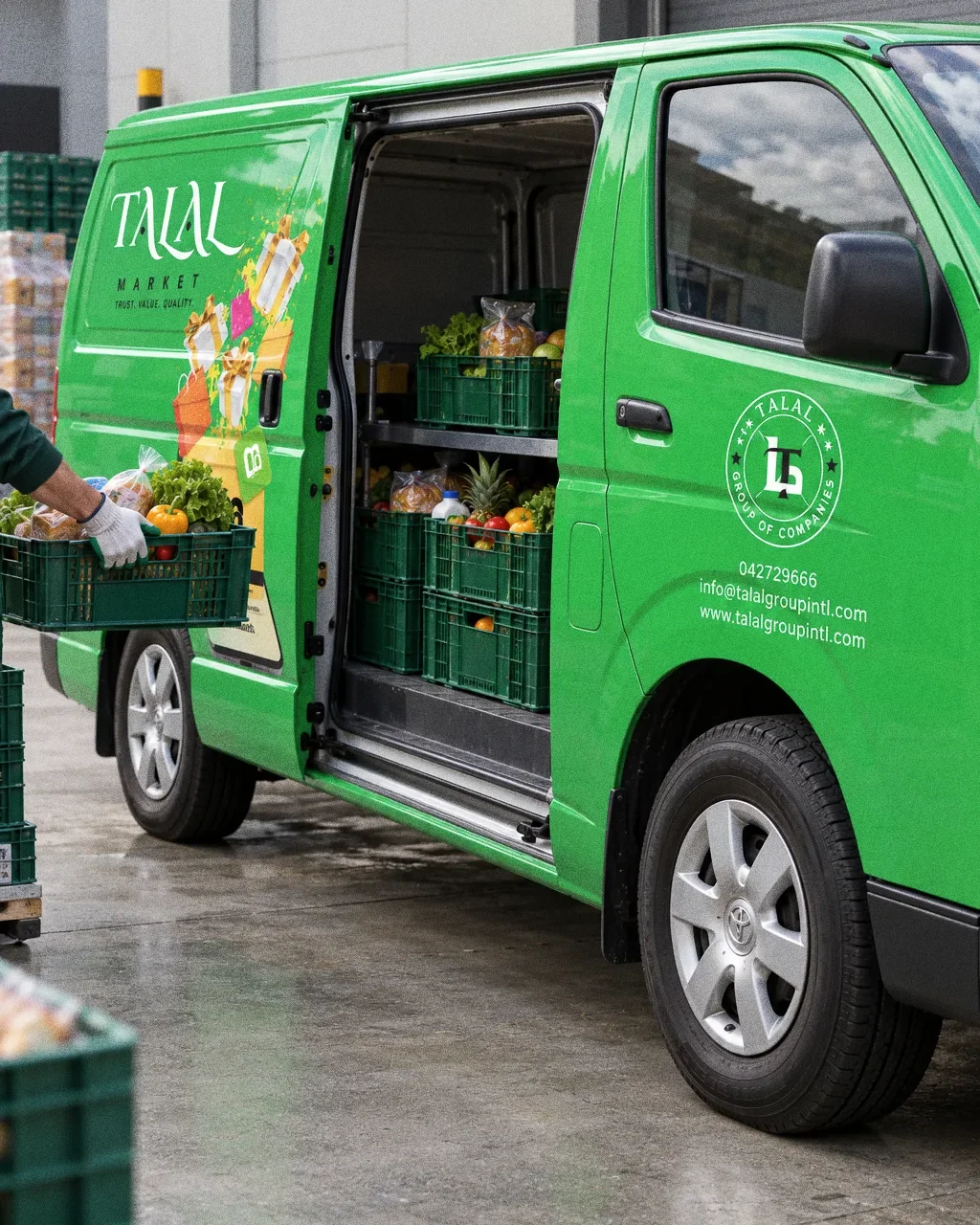 The sliding door of the Talal Market van open at a loading area, a gloved hand lifting a crate of groceries.